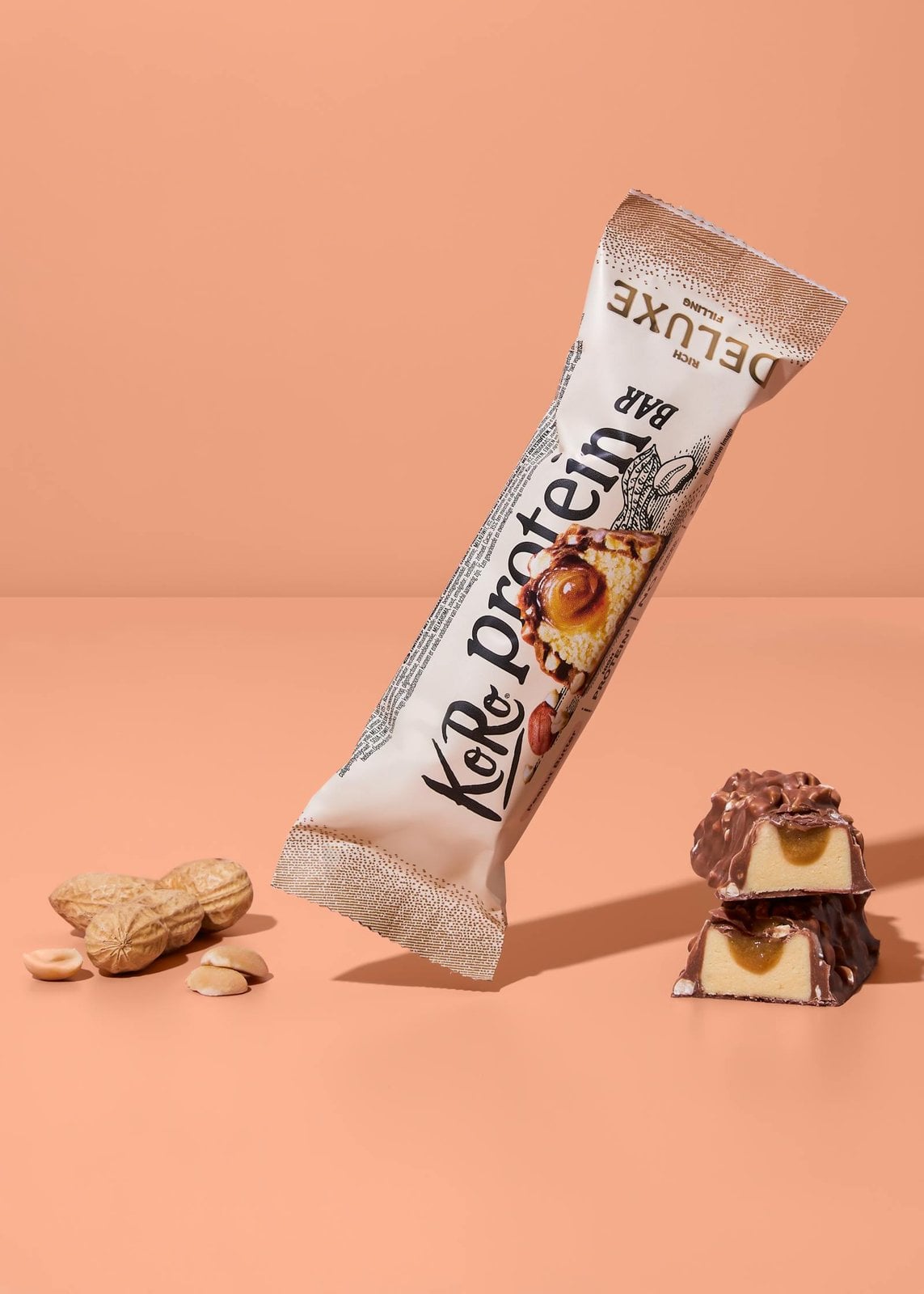 Proteinriegel von Korodrogerie mit Nüssen und angeschnittenem Riegel auf apricotfarbenem Hintergrund