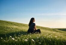 Woman sitting in a meadow beneath a broad sky